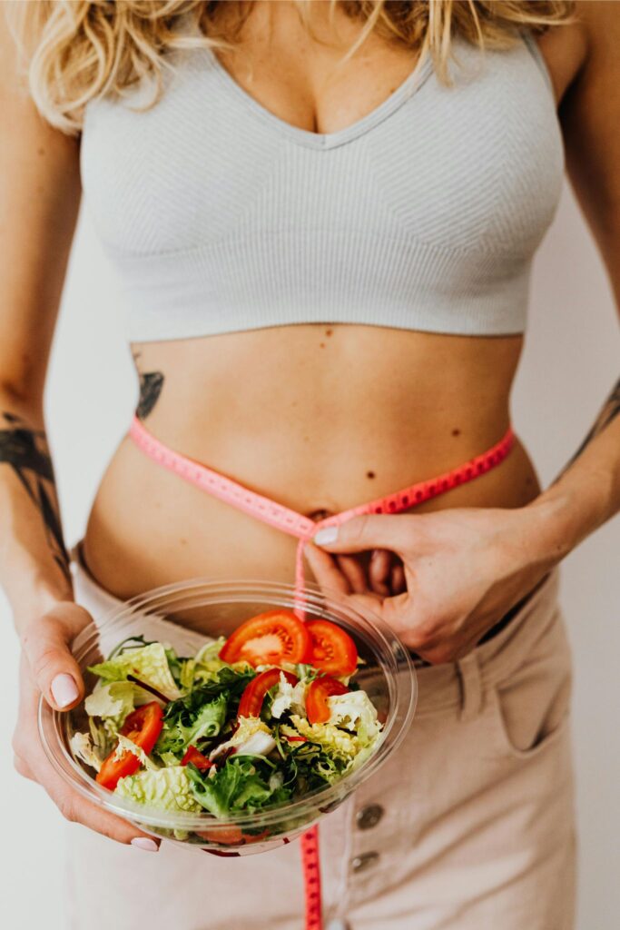 Mulher segurando uma fita métrica ao redor da cintura e um bowl de salada, representando acompanhamento nutricional para emagrecimento.
